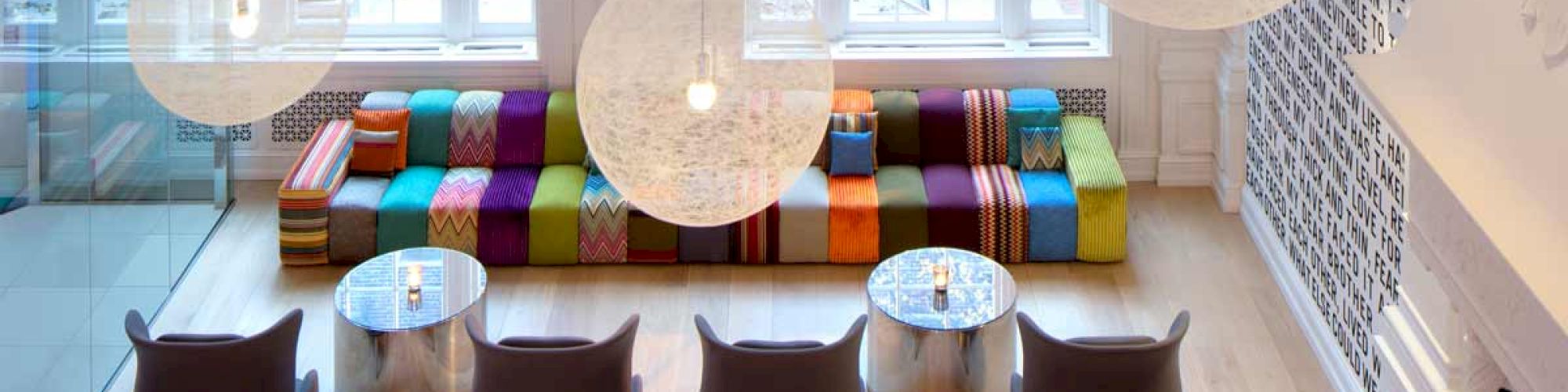 A modern lobby or lounge area with colorful seating, unique spherical light fixtures, large windows, and contemporary furniture.