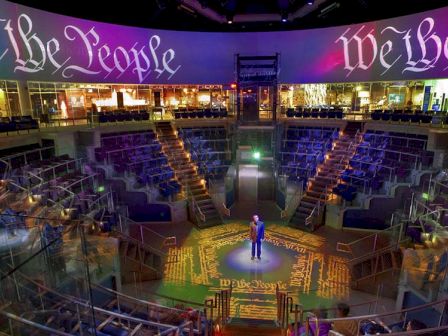 A person stands at the center of a circular stage surrounded by seating, with 