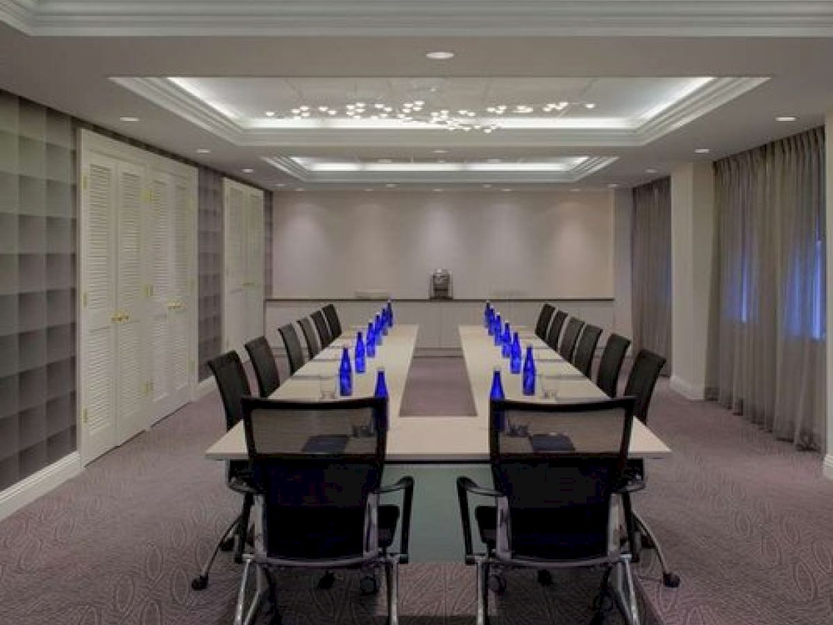 A modern conference room with a long table, office chairs, and blue glass bottles arranged neatly. The room has recessed lighting and grey curtains.